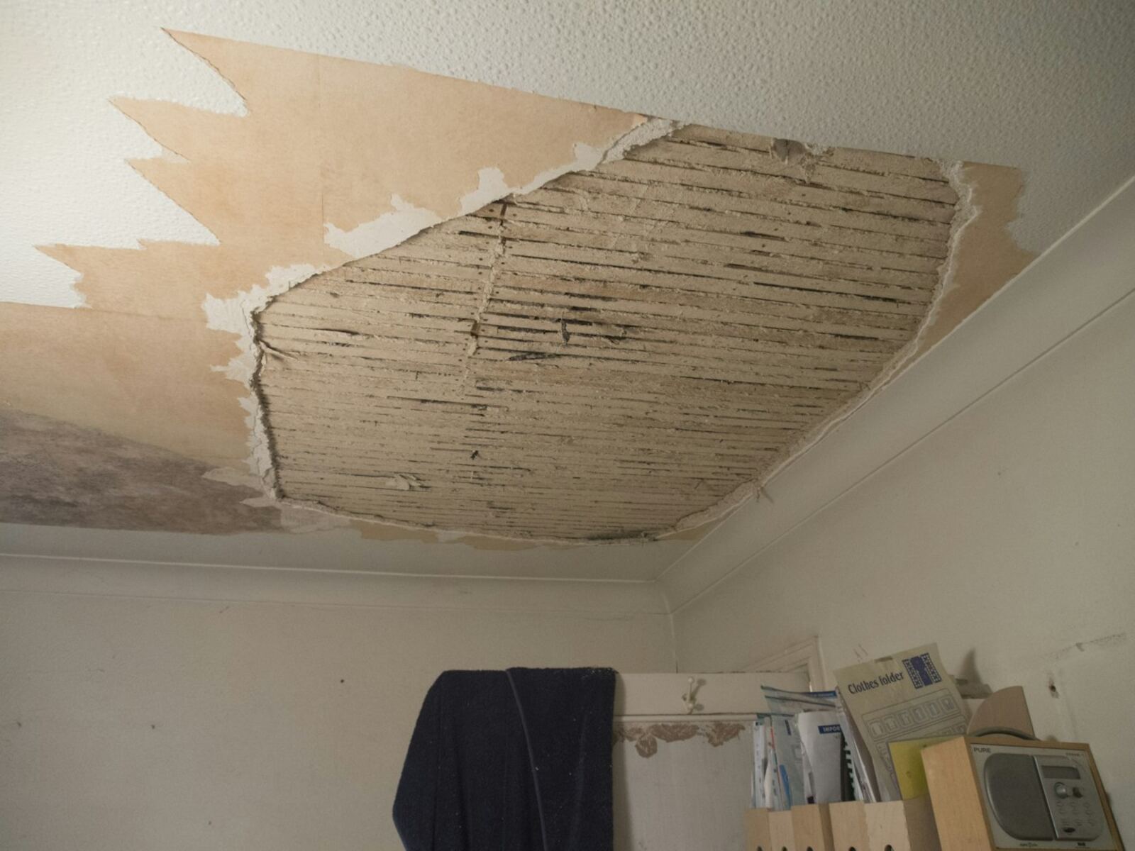 Plafond in een woonkamer waar het stucwerk door water is losgekomen en in stukken naar beneden is gevallen